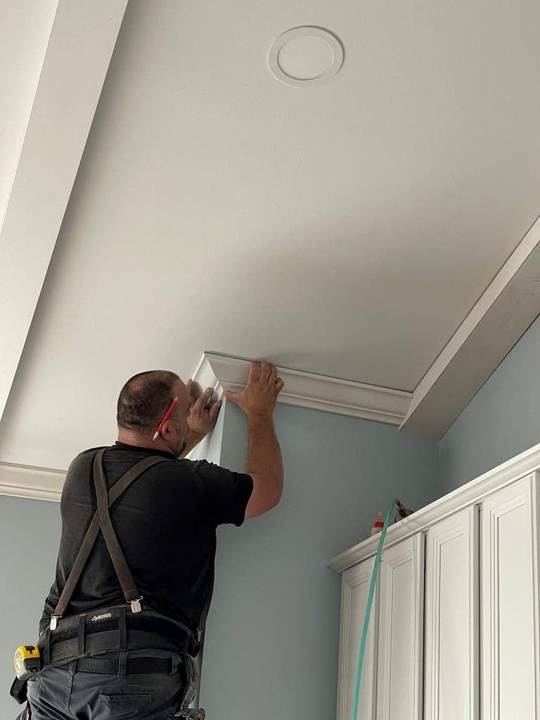 Professional finish carpenter carefully installing crown molding above custom built-ins